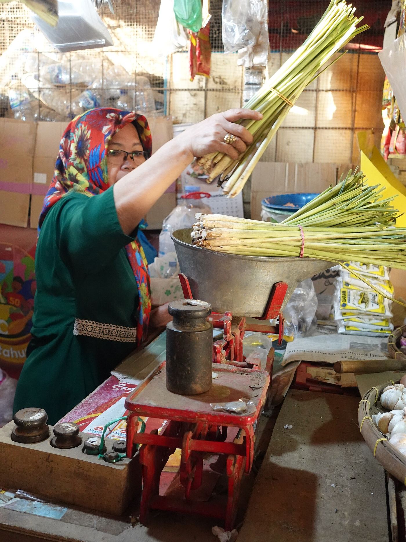 Ibu pemilik warung mengangkat seikat serai di atas timbangan
