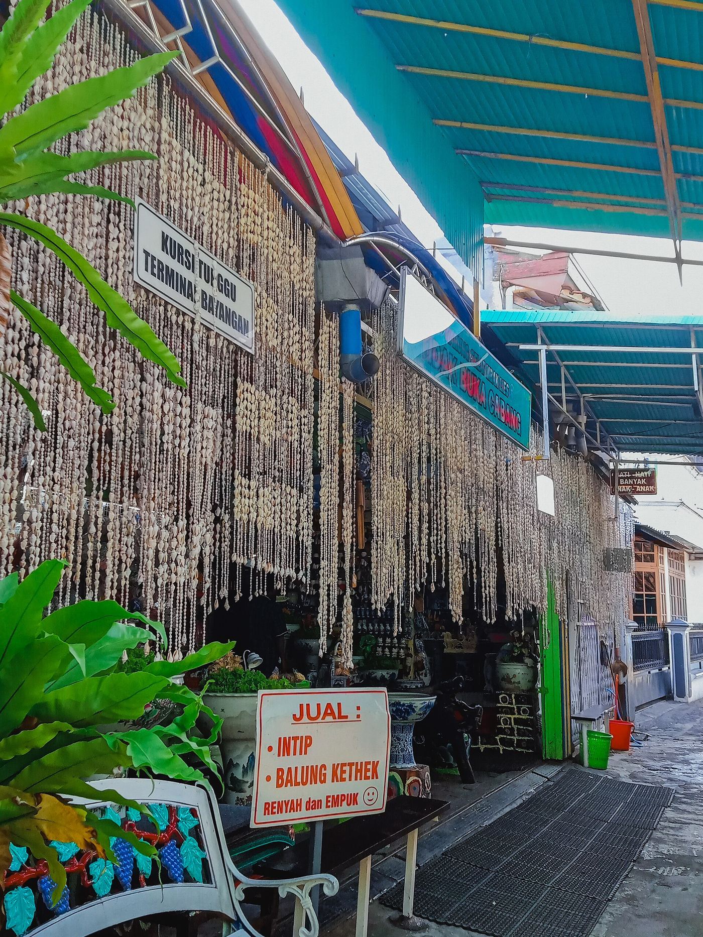 Lorong masuk warung di Solo dengan tirai kerang dan papan jualan